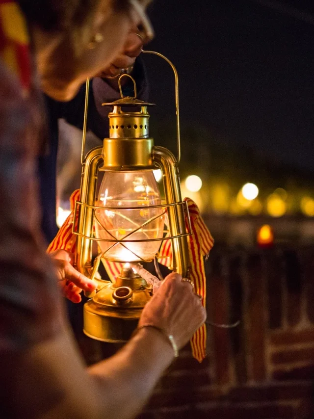 Personnes tenant une lanterne allumée ornée de rubans catalans lors de la fête de la Saint-Jean à Perpignan.