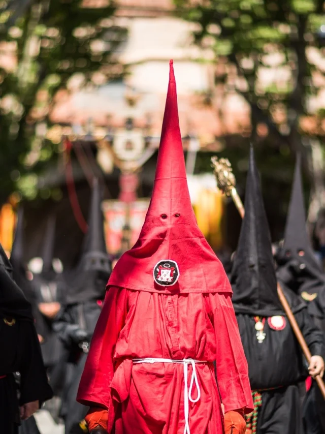 Pénitents vêtus de rouge et de noir défilant dans les rues de Perpignan lors de la Procession de la Sanch, sous le regard du public.