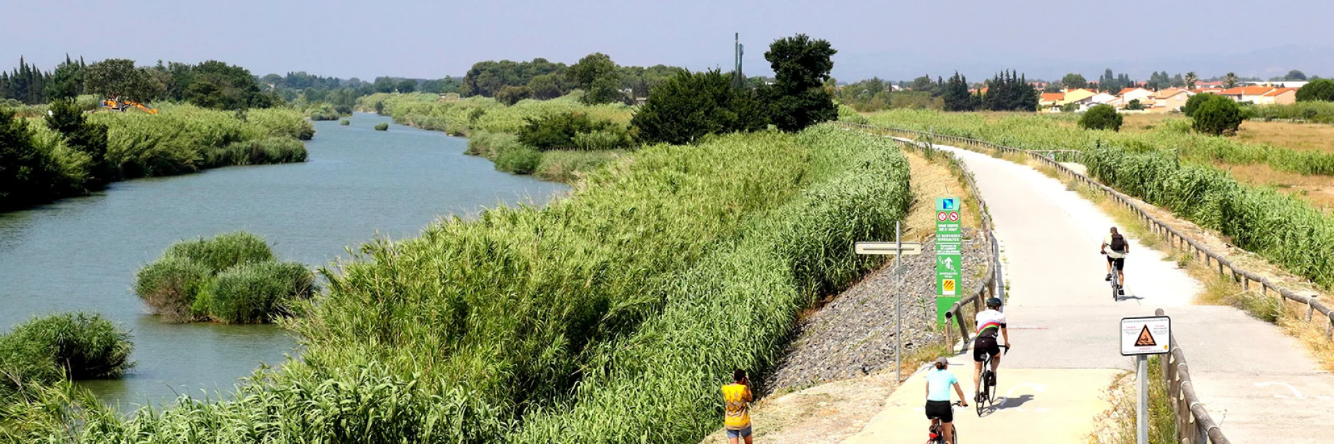 Cyclistes sur une voie verte longeant un cours d’eau entouré de végétation dense.