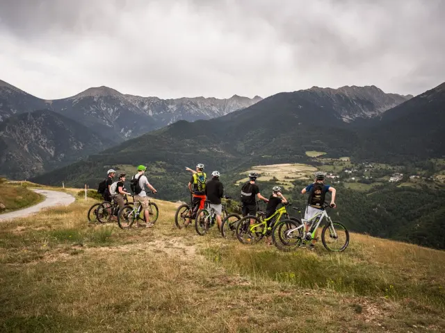 Groupe de cyclistes à VTT électrique arrêtés sur un plateau herbeux, observant un vaste panorama de montagnes et de vallées.